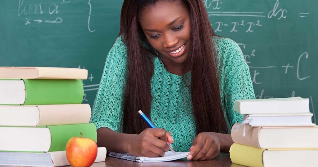 Una docente de raza negra escribiendo una nota en su escritorio.