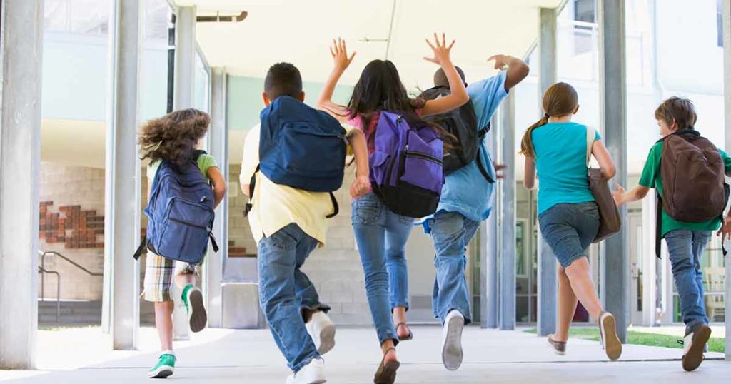 Una fila de niños con mochilas corriendo alegres hacia la escuela.