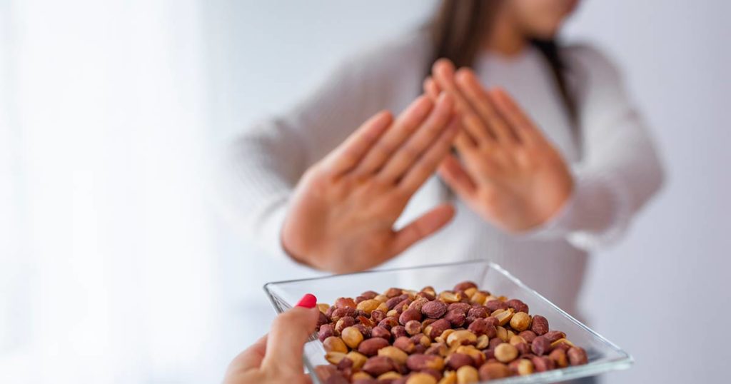 Mujer levantando las manos para rechazar nueces debido a una alergia alimentaria.