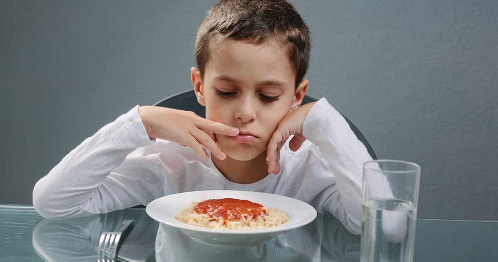 Niño con ansiedad ante la comida sentado frente a un plato de espaguetis.