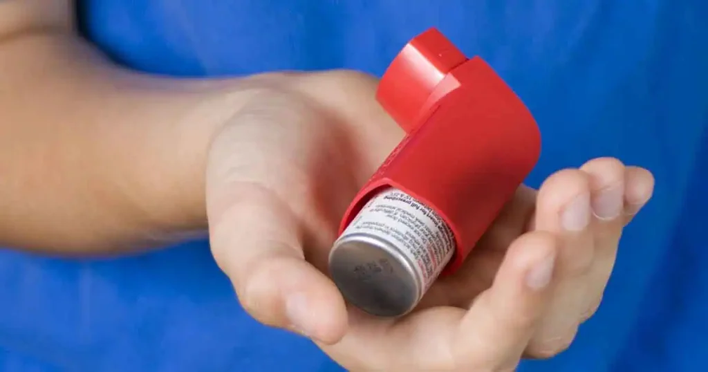 Una persona sostiene en la mano un inhalador rojo para el asma sobre un fondo azul.