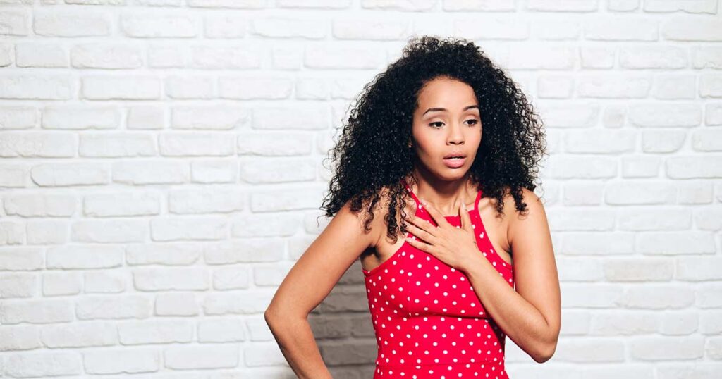 Una mujer con cabello rizado se sostiene el pecho mientras tiene un ataque de asma