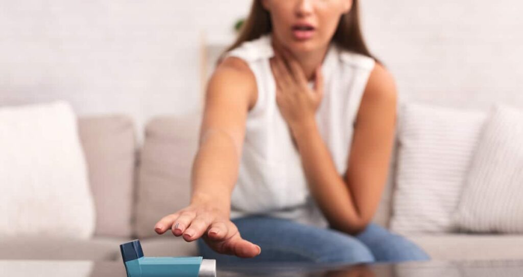 Joven sentada en un sofá en casa, tratando de alcanzar un inhalador para prevenir la depresión respiratoria