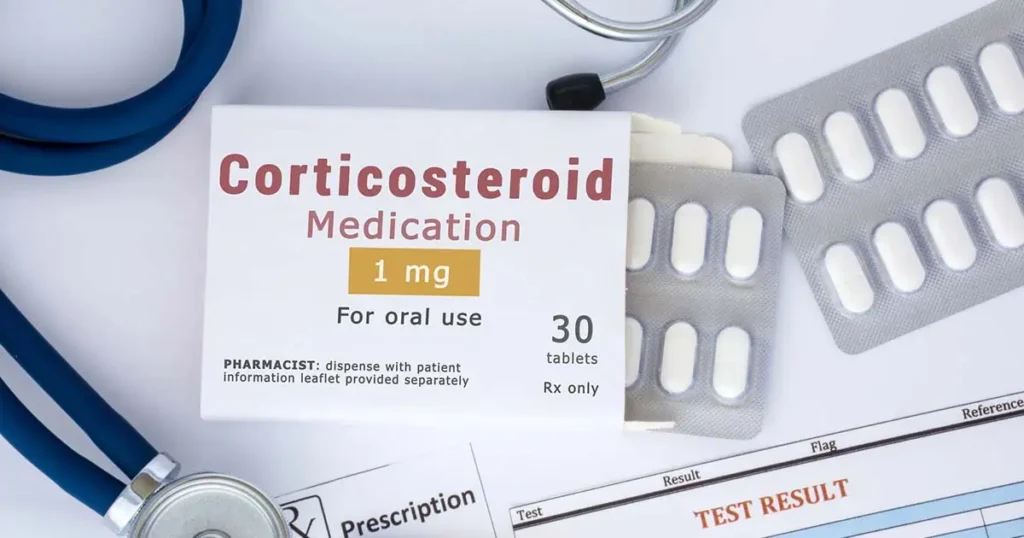 Una caja con la etiqueta "Medicamento corticosteroide 1 mg para uso oral" está sobre una mesa junto a tabletas, un estetoscopio, recetas médicas y un documento marcado como "RESULTADO DE PRUEBA".